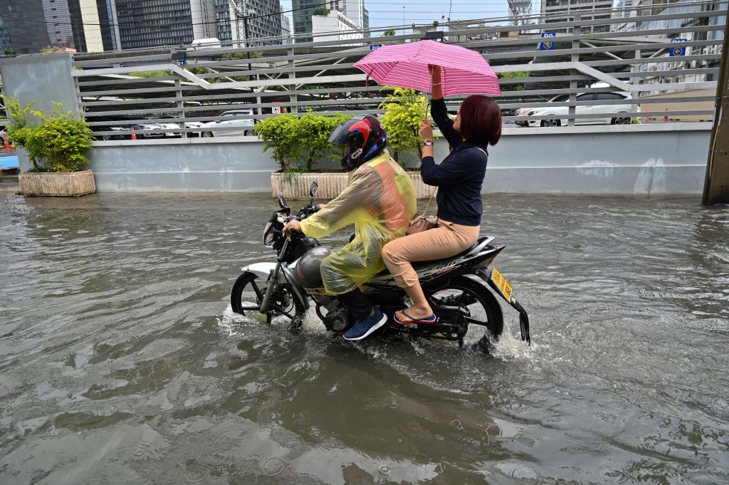 TOPSHOT - A woman adjusts her umbrella while riding a motorcycle taxi through a flooded street after heavy rain in Bangkok on June 7, 2019. (Photo by Romeo GACAD / AFP)        (Photo credit should read ROMEO GACAD/AFP/Getty Images)