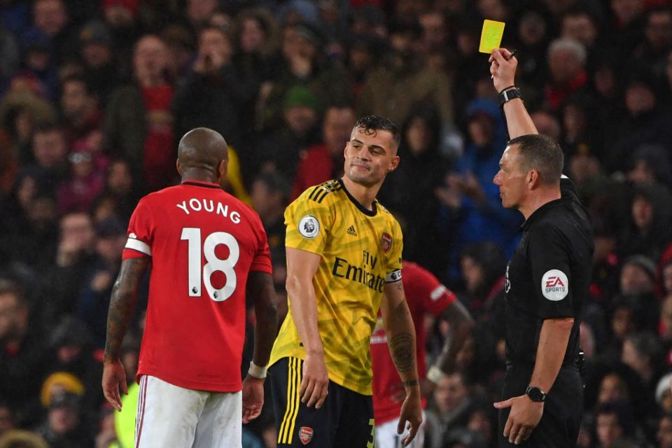 Arsenal's Swiss midfielder Granit Xhaka (C) is booked by English referee Kevin Friend (R) as Manchester United's English defender Ashley Young (L) looks on during the English Premier League football match between Manchester United and Arsenal at Old Trafford in Manchester, north west England, on September 30, 2019. (Photo by Paul ELLIS / AFP) / RESTRICTED TO EDITORIAL USE. No use with unauthorized audio, video, data, fixture lists, club/league logos or 'live' services. Online in-match use limited to 120 images. An additional 40 images may be used in extra time. No video emulation. Social media in-match use limited to 120 images. An additional 40 images may be used in extra time. No use in betting publications, games or single club/league/player publications. /         (Photo credit should read PAUL ELLIS/AFP/Getty Images)